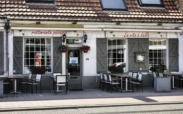 The white façade of La Vita è Bella with grey shutters, red geraniums and terrace