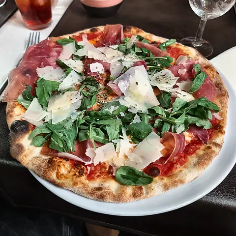 Pizza with Parma ham, rocket and shaved grana on a white plate